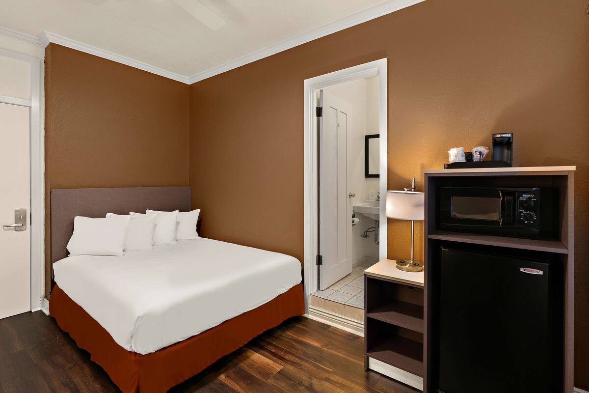 A hotel room with a bed, a microwave, a refrigerator, and a door leading to a bathroom.