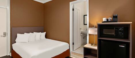 Una habitación de hotel con una cama, microondas, refrigerador y puerta que da a un baño.