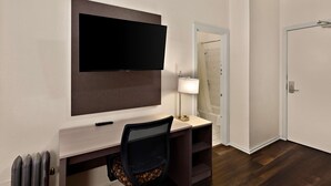 A hotel room with a flat-screen TV mounted on the wall, a desk with a chair, a lamp, and a shower visible through an open door. - Mithila San Francisco, SureStay Collection by Best Western (San Francisco)