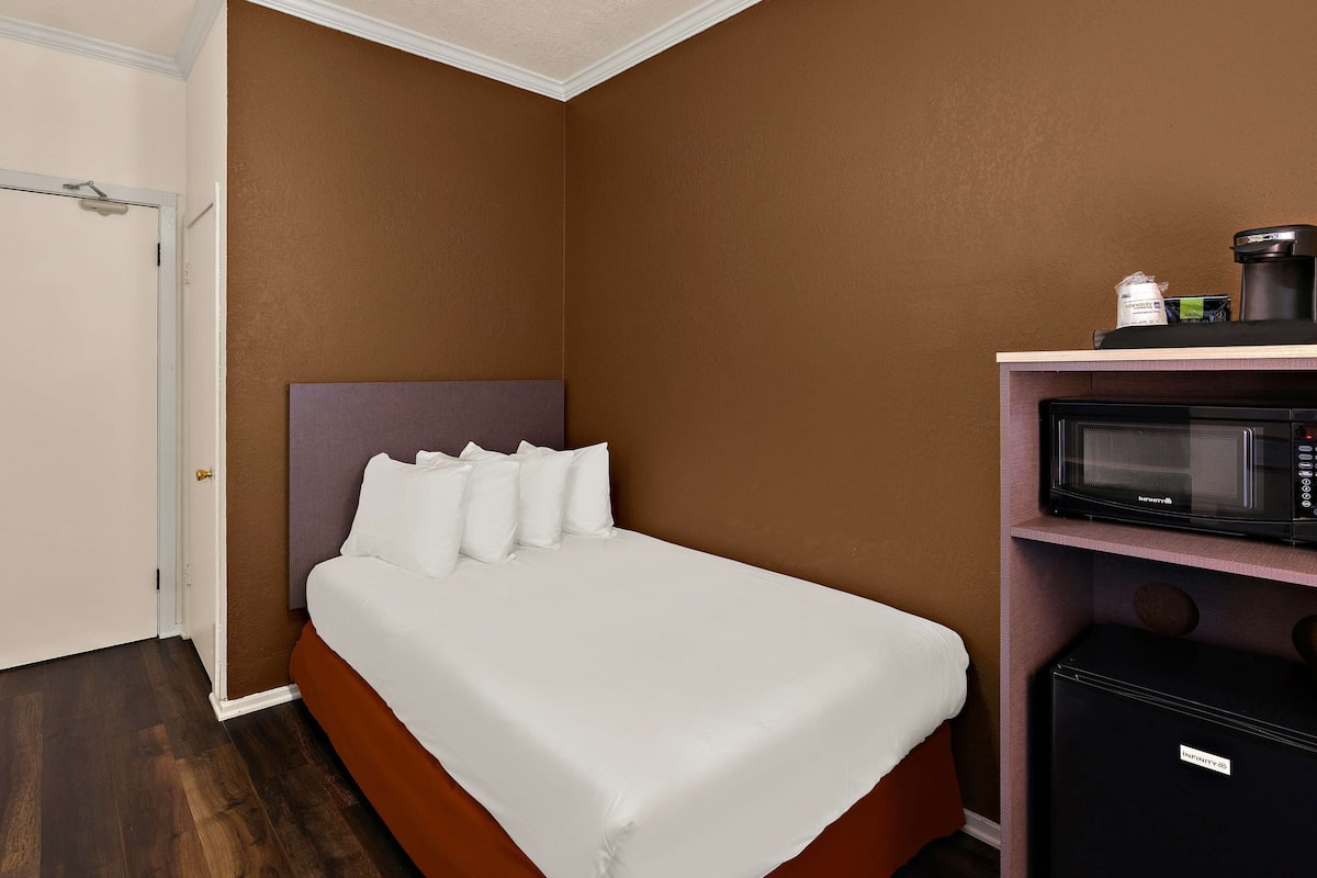 A hotel room with a bed, a microwave, and a coffee maker on a shelf.