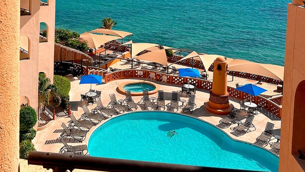 Un resort con piscina, sillones de descanso y vistas al mar.