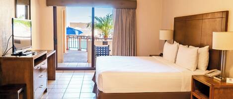 Una habitación de hotel con cama, escritorio, televisor y balcón con vistas.