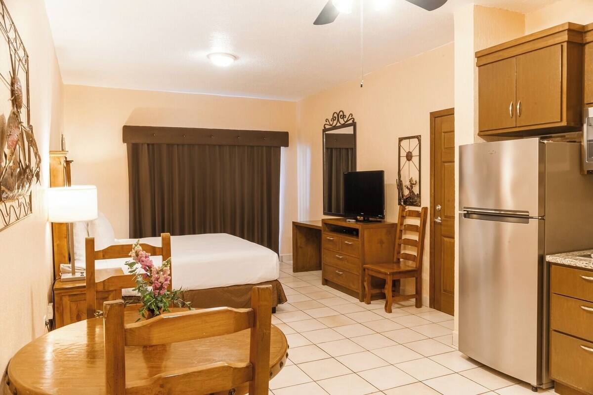 Habitación de hotel con cama, escritorio con televisor, refrigerador y zona de comedor con mesa y sillas.