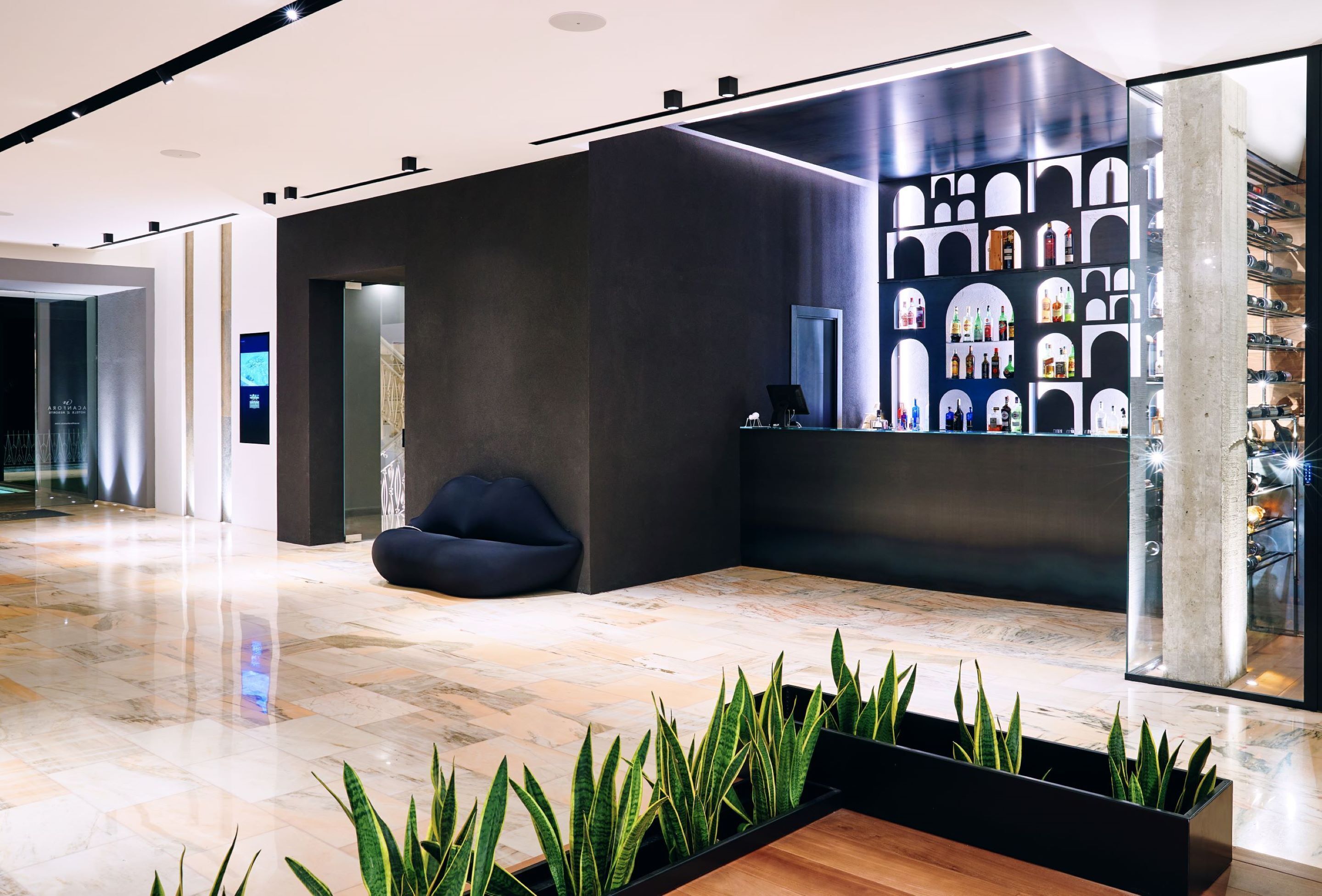 A modern lobby with a reception desk, seating area, and a display of bottles.