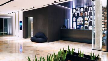 A modern lobby with a reception desk, seating area, and a display of bottles.