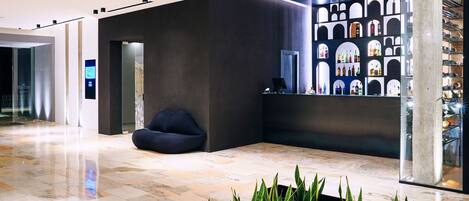 A modern lobby with a reception desk, seating area, and a display of bottles.