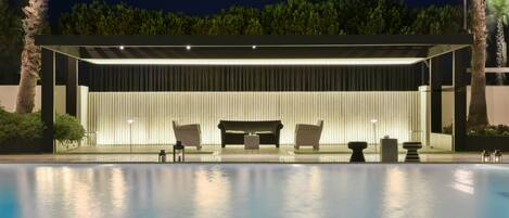 A modern outdoor pool area with a covered seating area, a pool, and surrounding greenery.