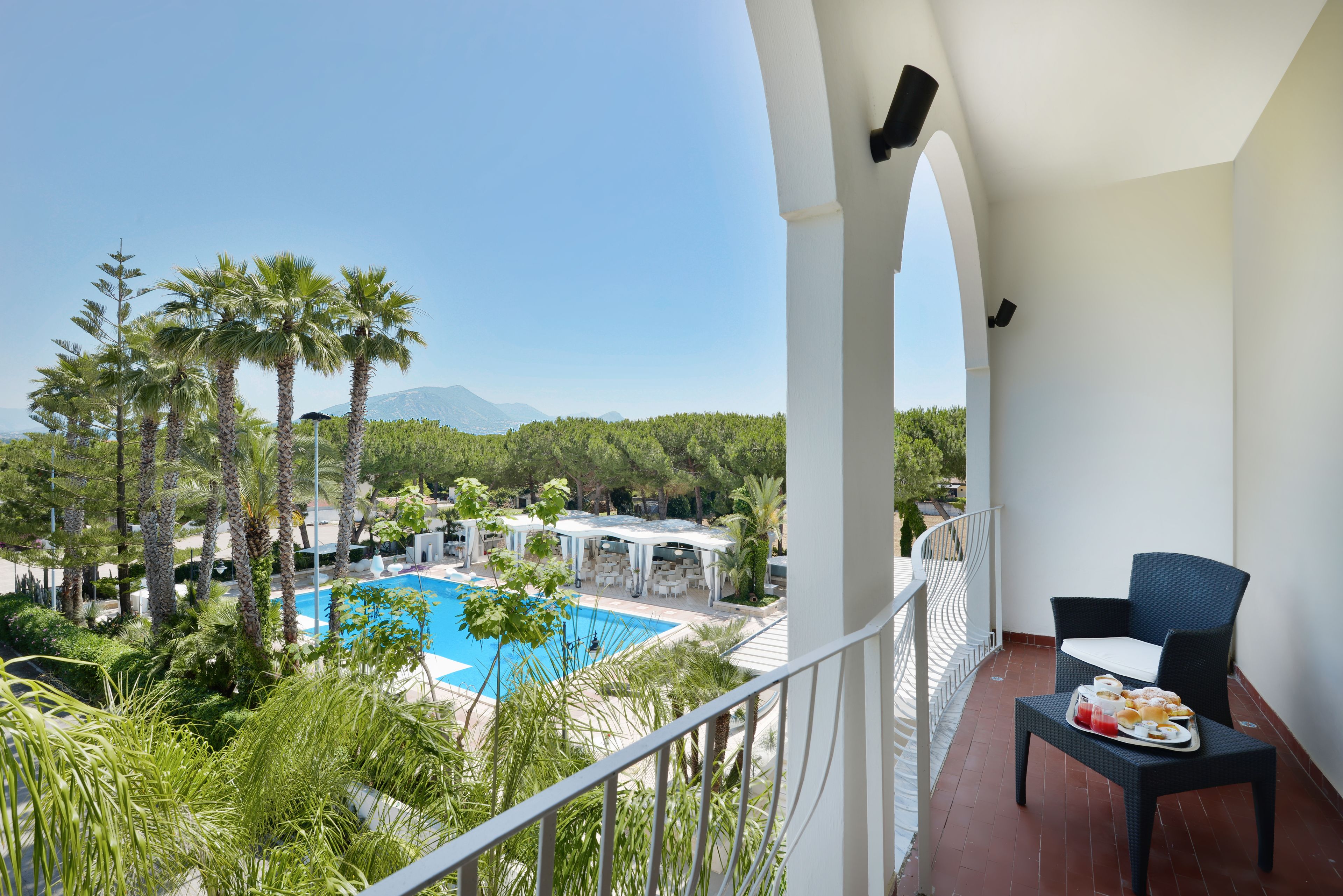 A balcony with a view of a pool, palm trees, and a mountain in the background.