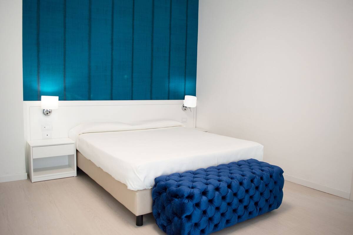 A bedroom with a bed, bedside tables, and a blue upholstered bench.