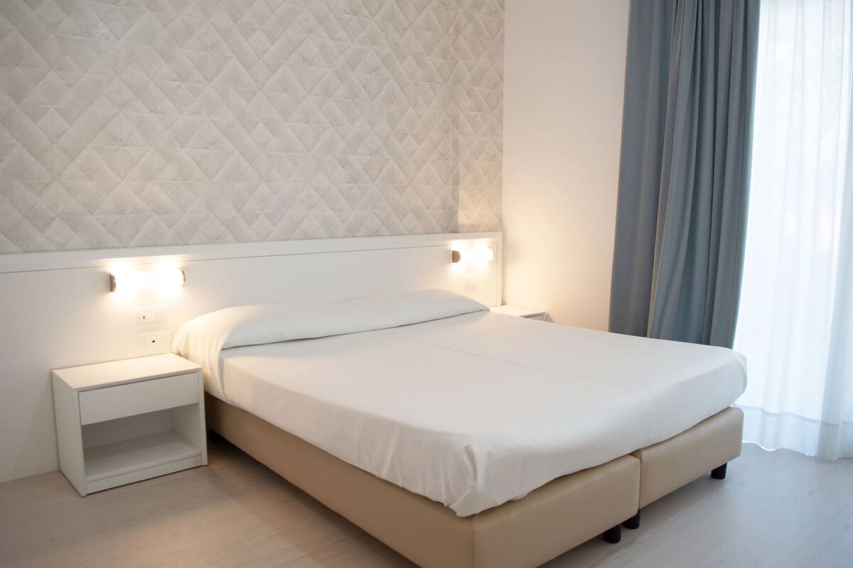 A bedroom with a bed, nightstand, and wall-mounted light.