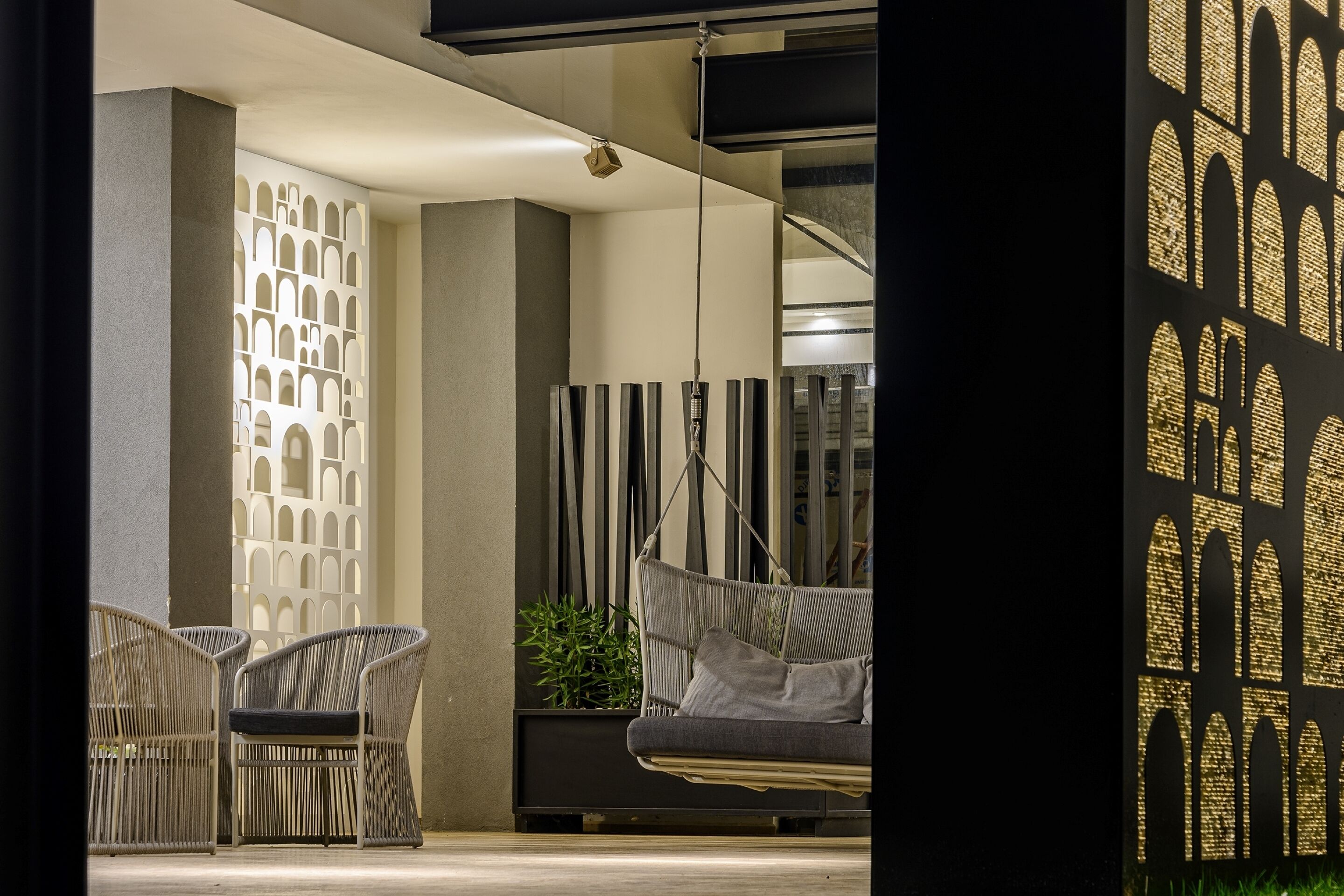 A modern outdoor seating area with wicker chairs and a hanging swing, a decorative wall with geometric patterns, and a potted plant.