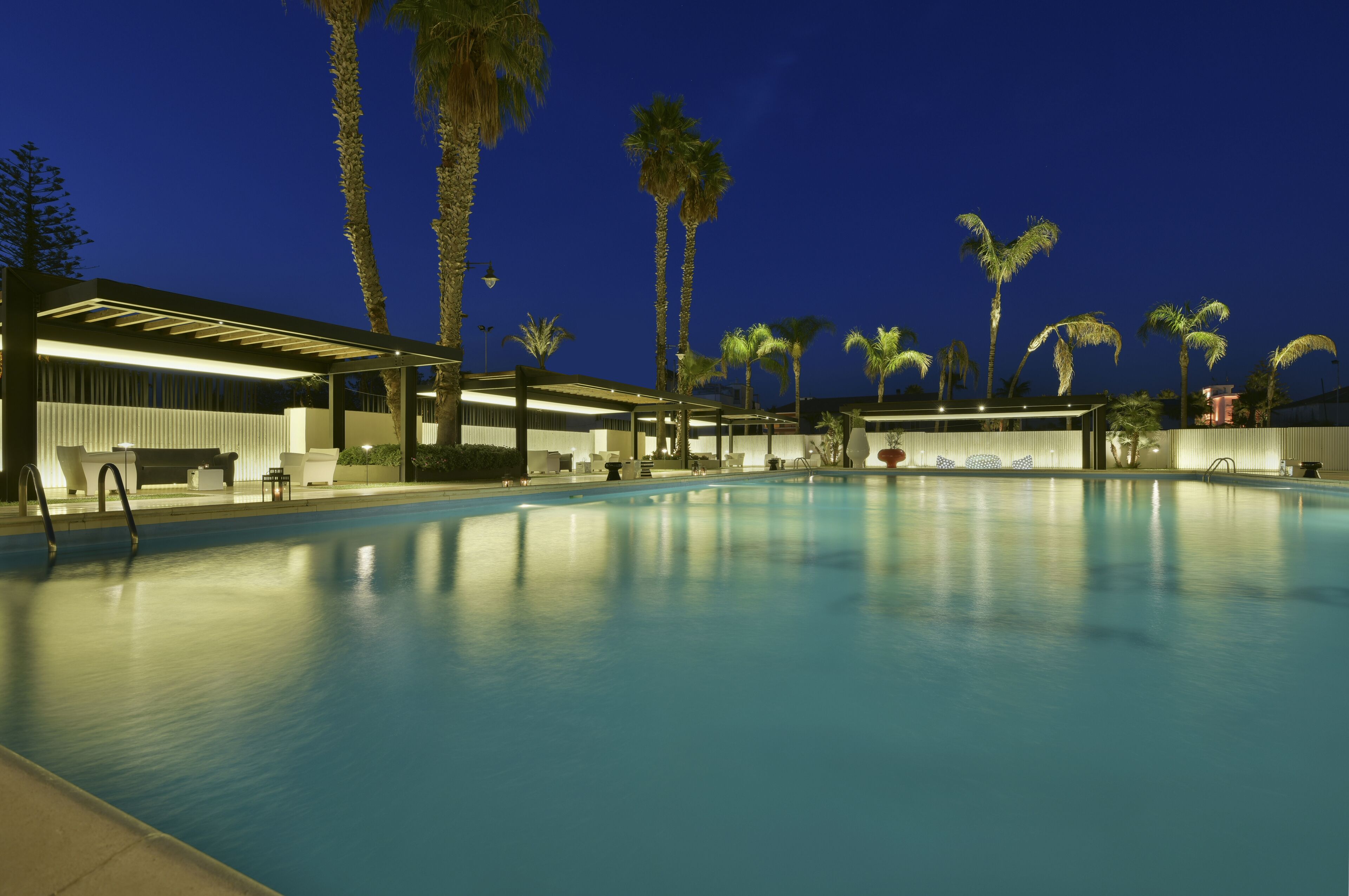 A swimming pool area with a covered seating area and palm trees.