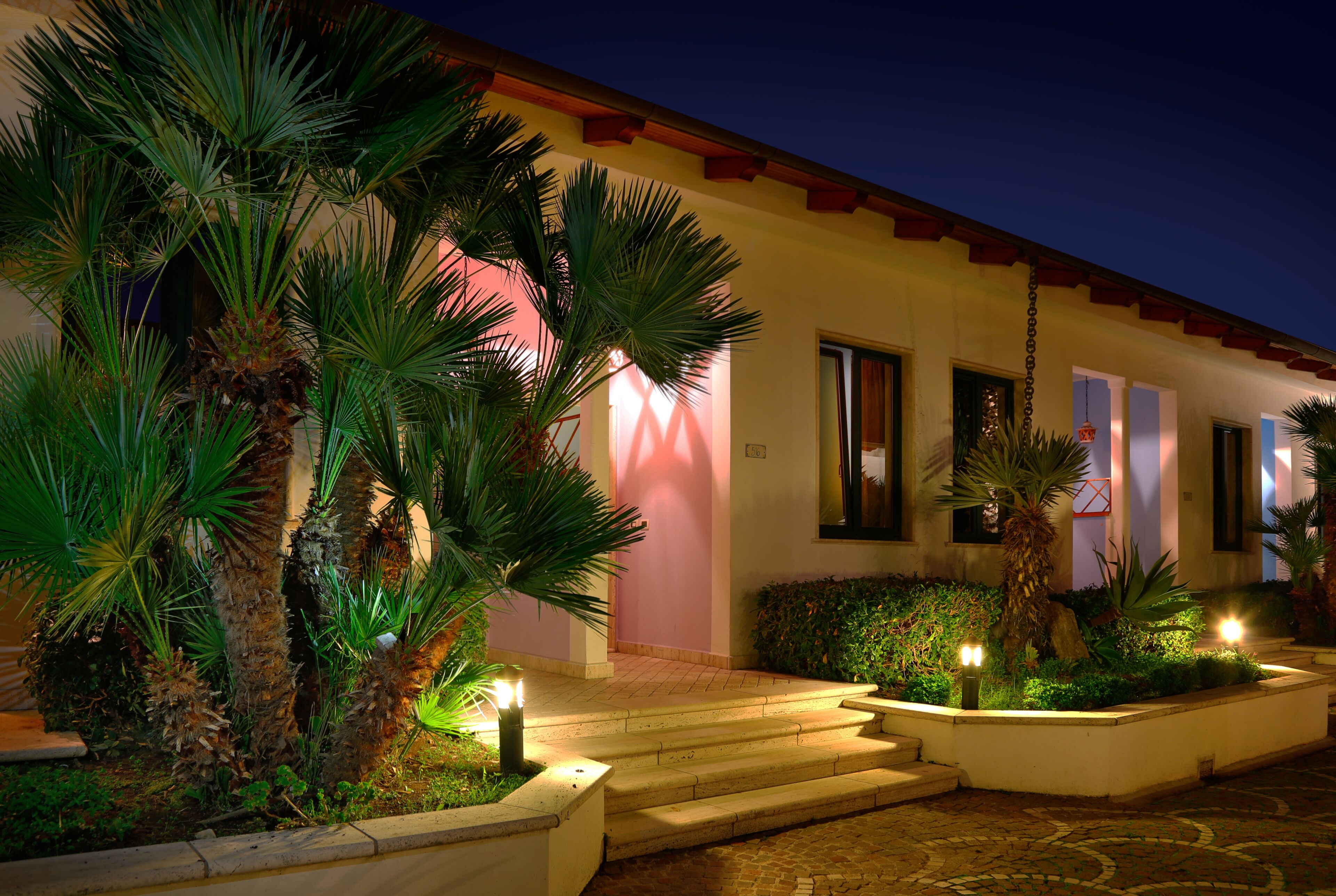 A building with a red-tiled roof, a pink wall, and a well-lit entrance with steps leading up to it.