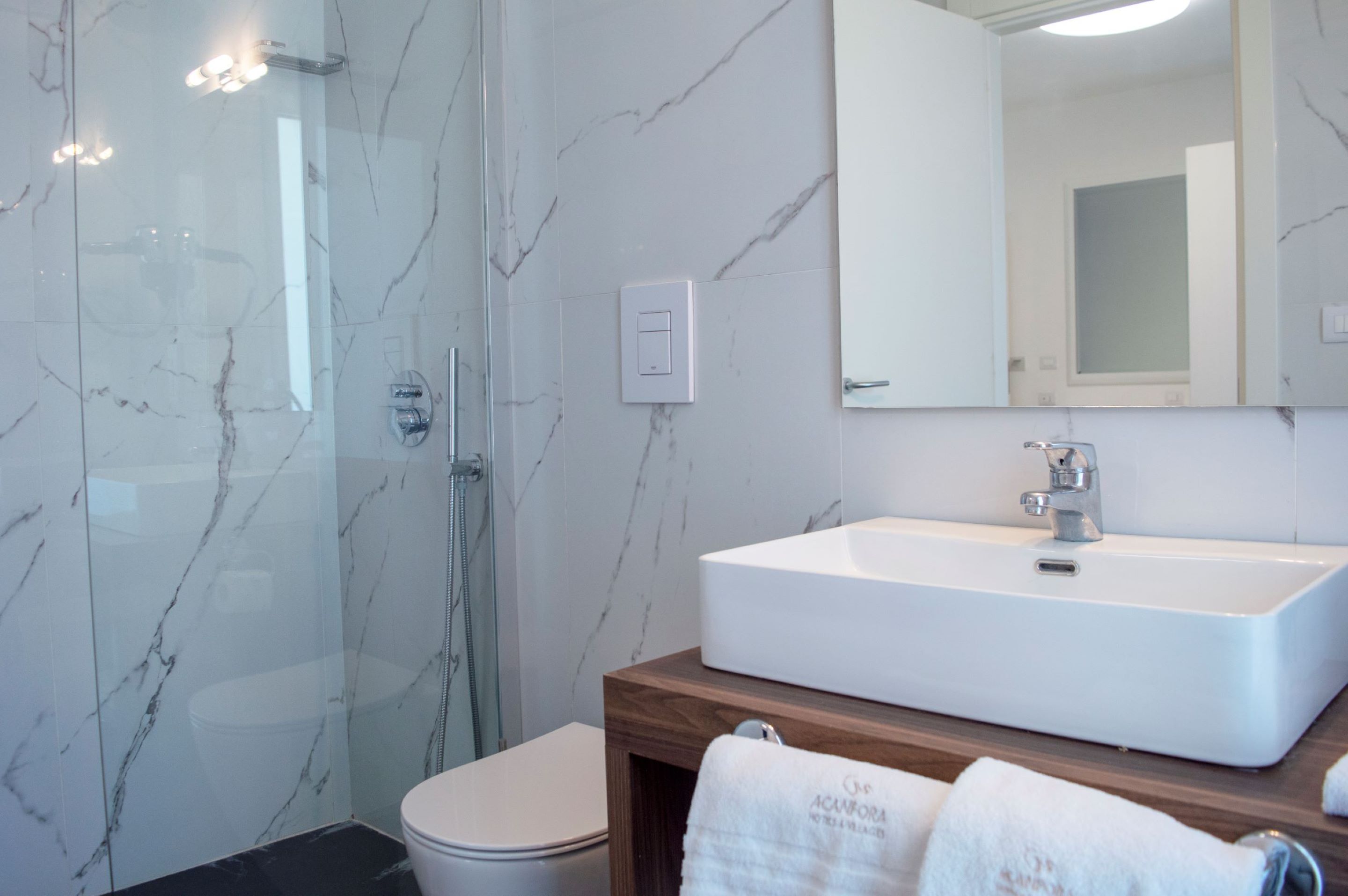 A bathroom with a glass-enclosed shower, a white sink, and a wooden vanity.