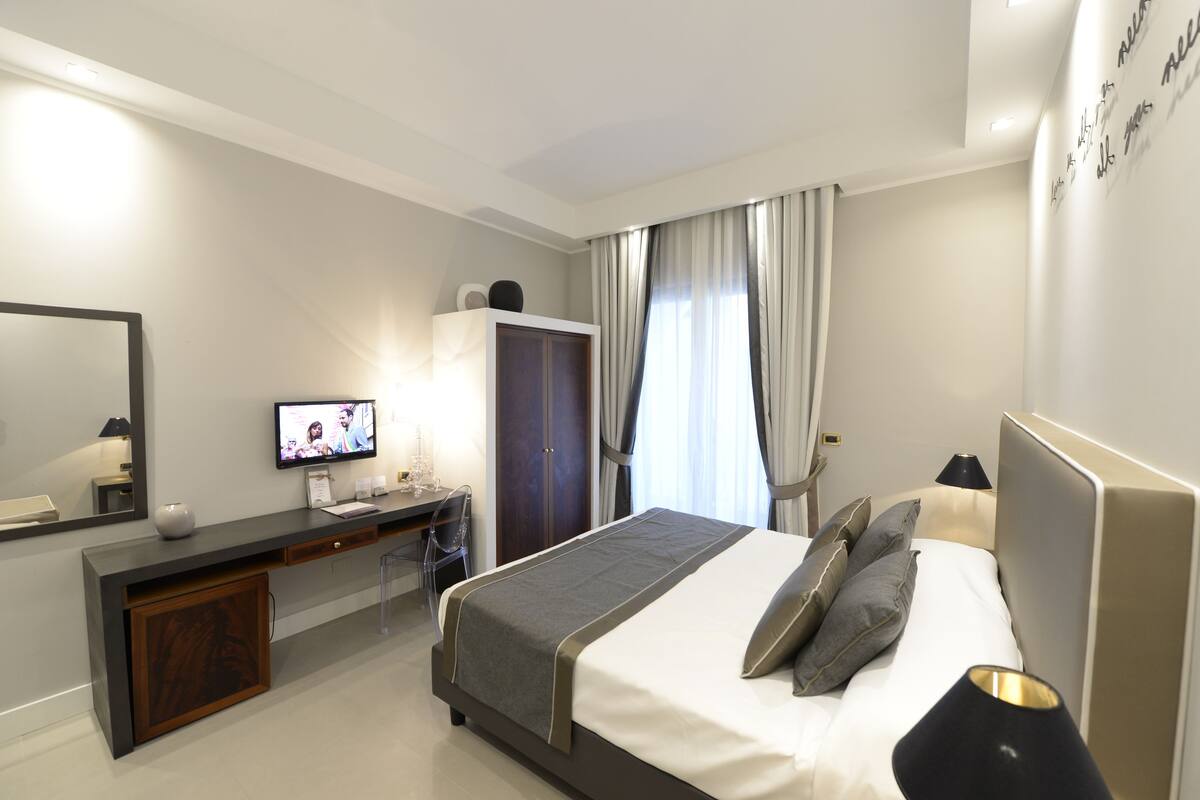 A modern hotel room with a bed, a desk, a TV, and a wardrobe.