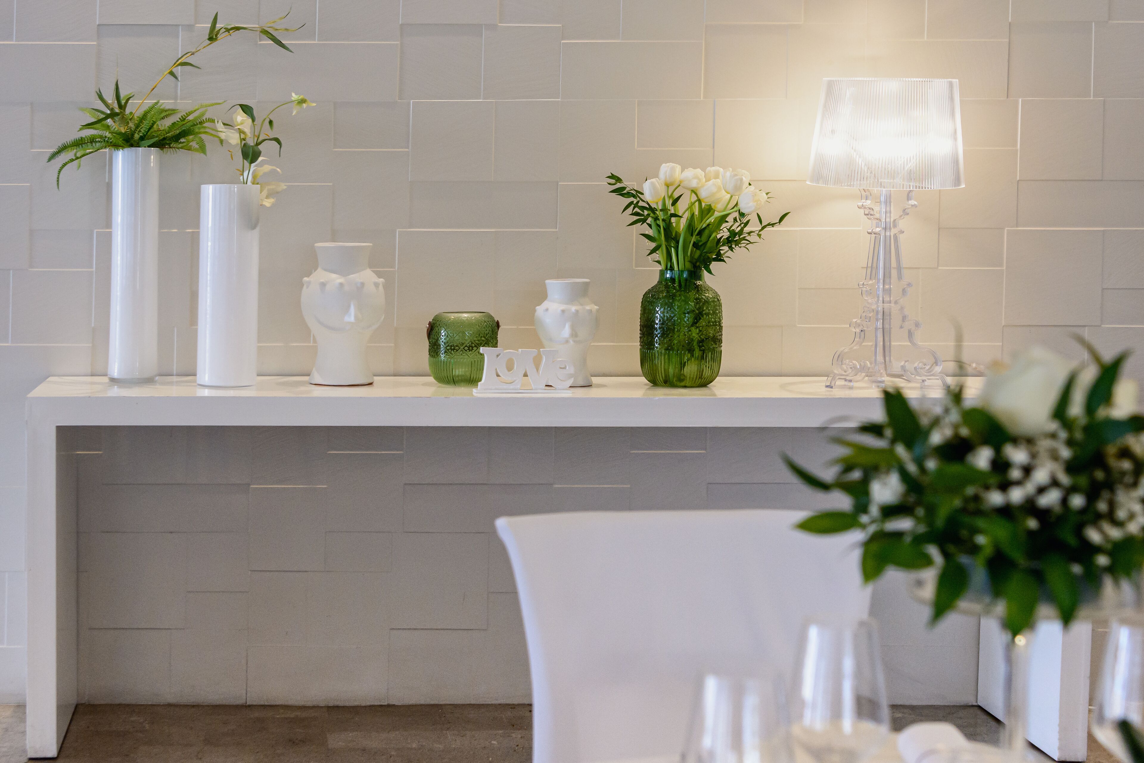 A reception area with a white reception desk, a green vase with white flowers, a white vase with green leaves, and a white vase with white flowers.