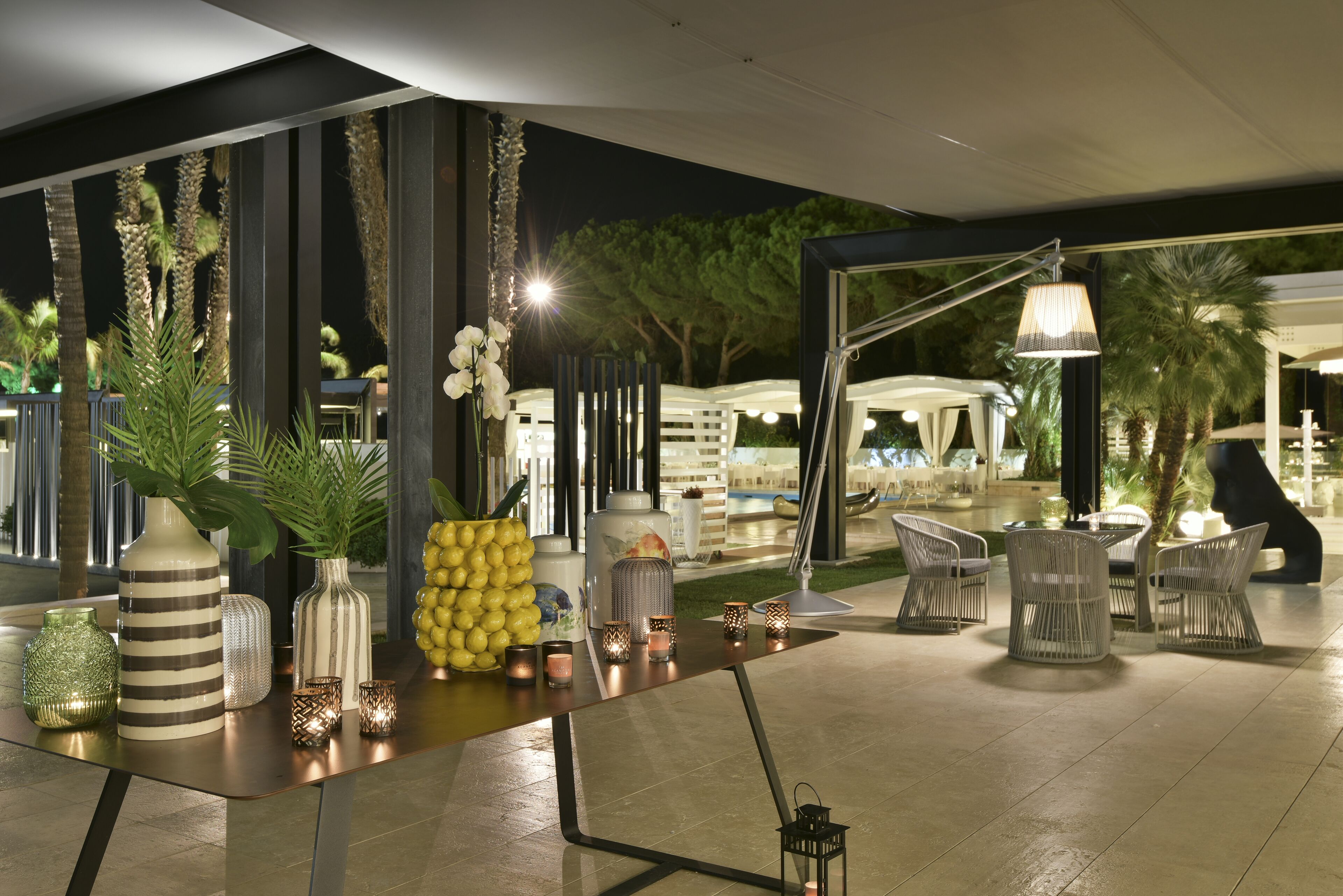 An outdoor dining area with a long table, chairs, and decorative vases.