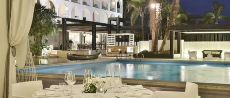 A hotel with a pool, outdoor seating, and a white facade.