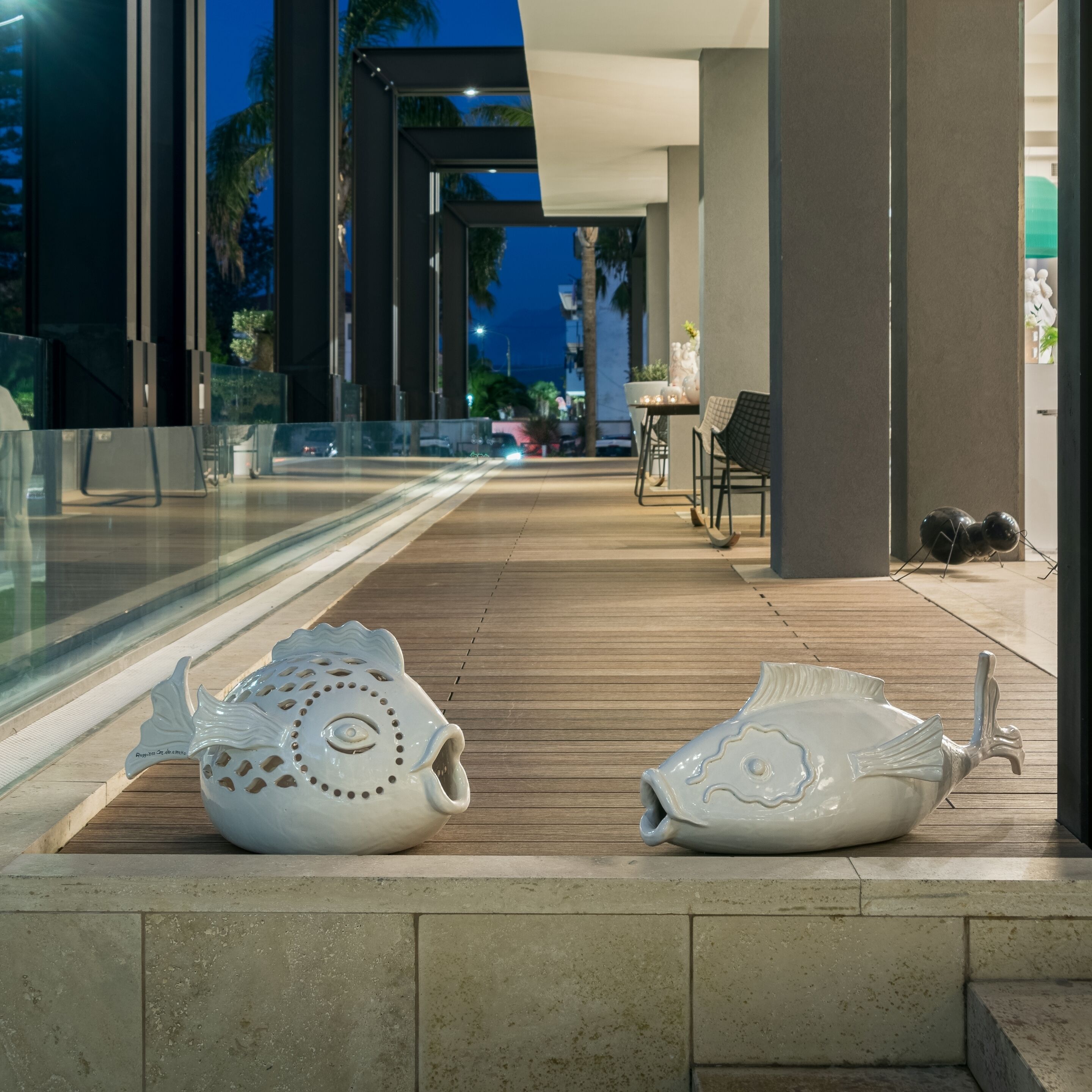 A modern outdoor area with a wooden deck, two decorative fish sculptures, and a glass railing.