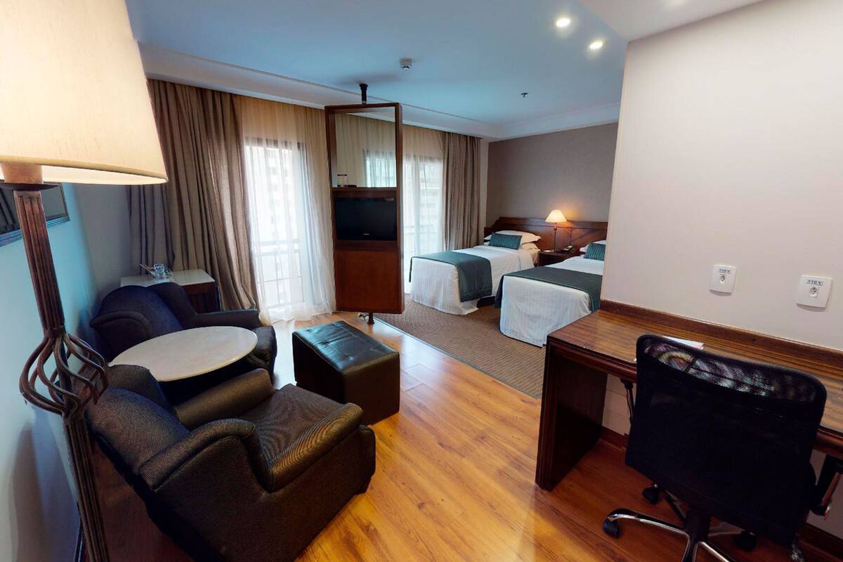 A hotel room with a sofa, a desk, a chair, a bed, and a TV.