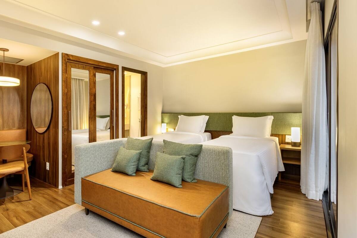 A hotel room with a wooden floor, a sofa, two beds, a mirror, and a desk.