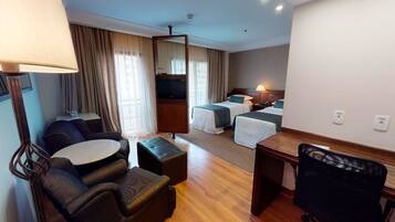 A hotel room with a sofa, a small table, a desk, a chair, a bed, and a TV.