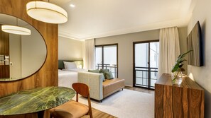 A hotel room with a bed, a sitting area, a dining table, a mirror, and a television. - Estanplaza Paulista (São Paulo)