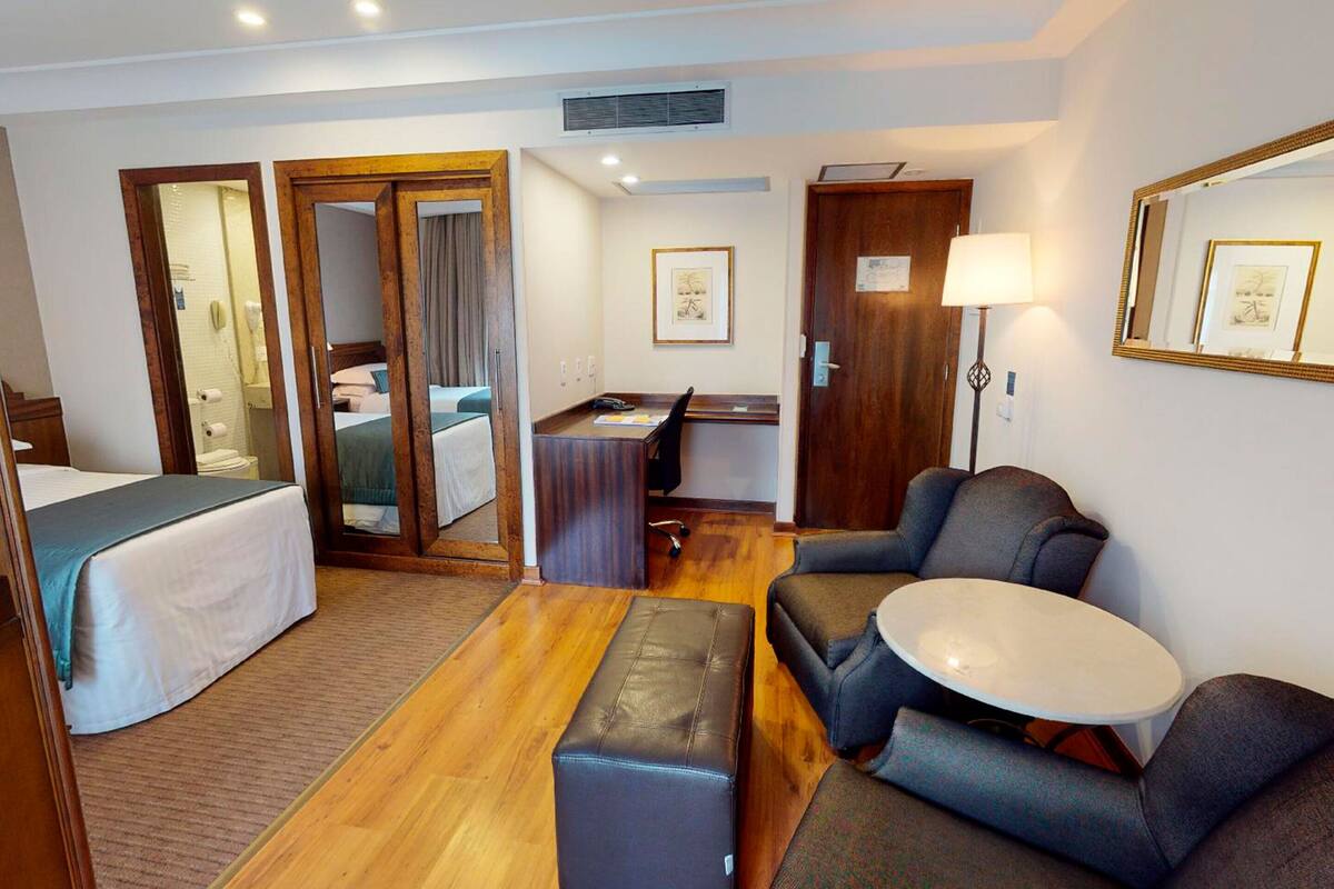 A hotel room with a bed, a desk, a sofa, a small table, and a mirror.