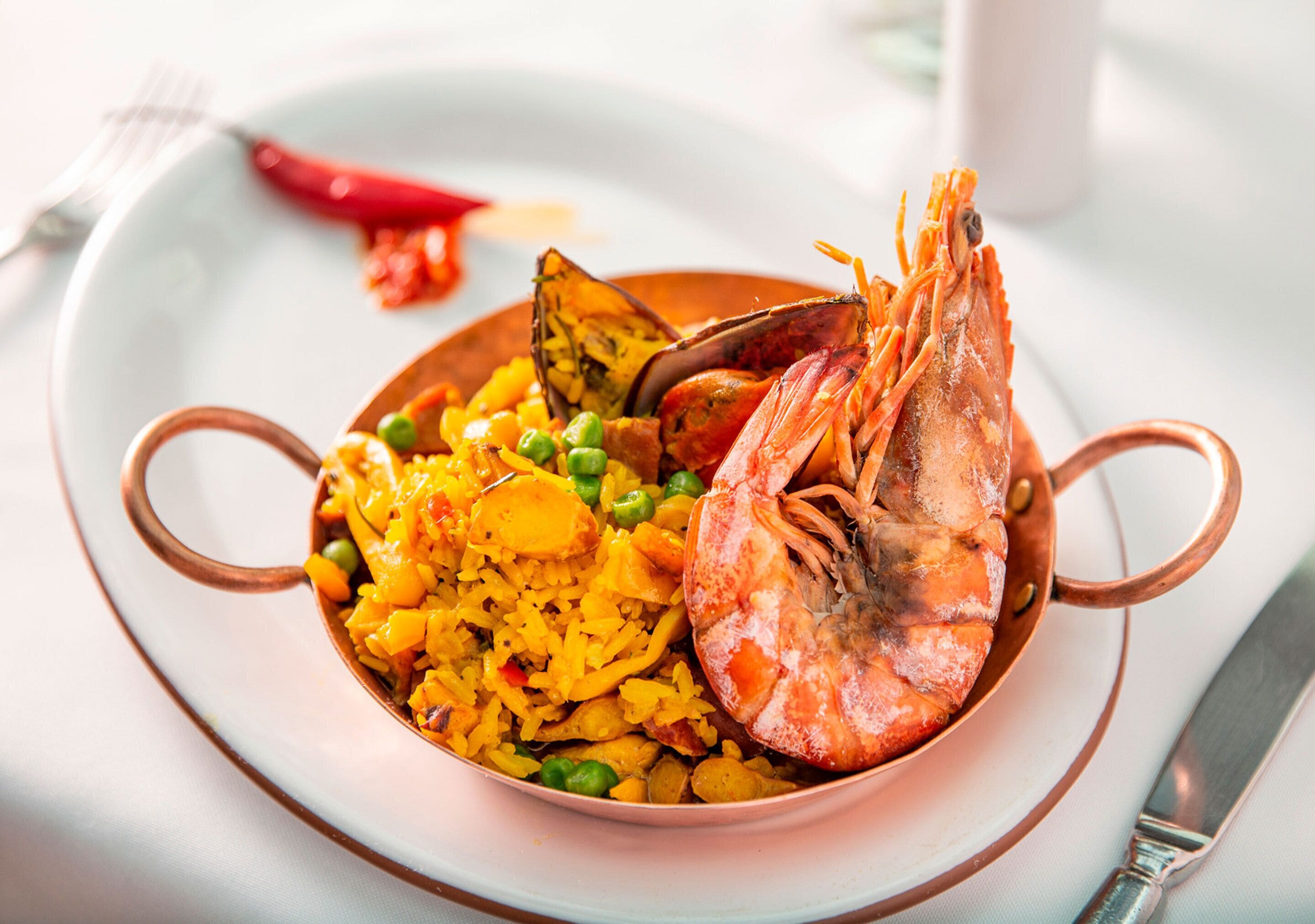 A bowl of rice with peas and shrimp, served on a plate with a copper handle.
