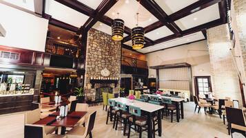A spacious restaurant with high ceilings, exposed beams, and a stone fireplace. Tables and chairs are arranged for dining.
