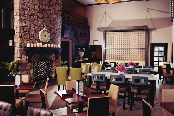 A restaurant with stone walls, a clock, and multiple dining tables with chairs.