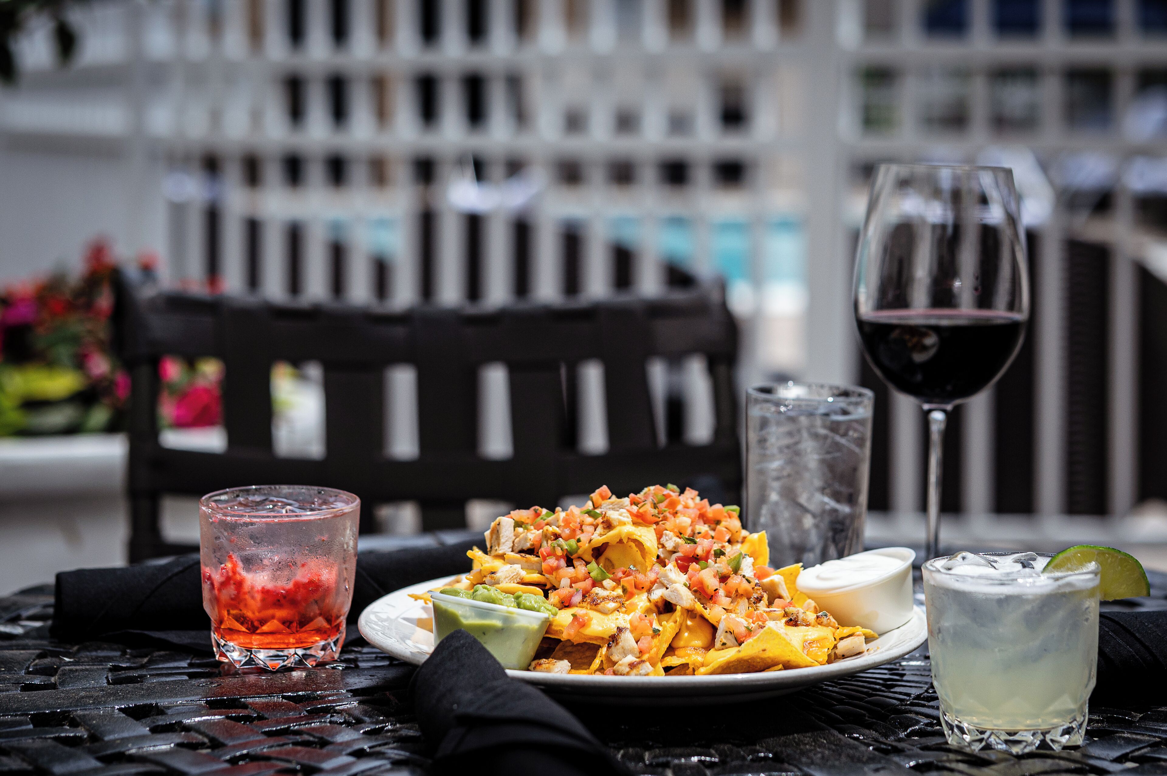 En tallerken med nachos, en drik og et glas rødvin på et bord.