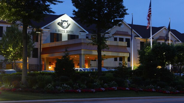 A hotel with a prominent sign reading "A SUTE HOTEL" and multiple flags, including the American flag, in front. - The Inn At Fox Hollow Hotel (Woodbury)
