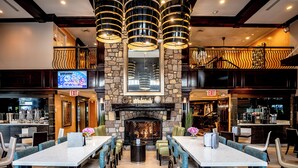 A restaurant with a stone fireplace, multiple tables, and chairs. There are two visible exits and a television on the wall. - The Inn At Fox Hollow Hotel (Woodbury)