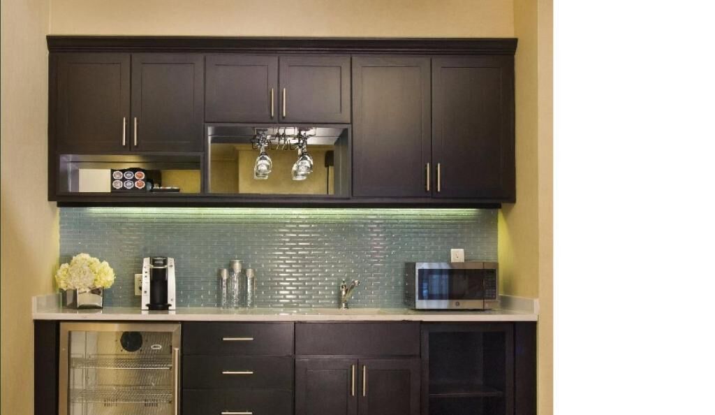 A kitchen with dark cabinets, a stainless steel microwave, a coffee maker, and a glass backsplash.