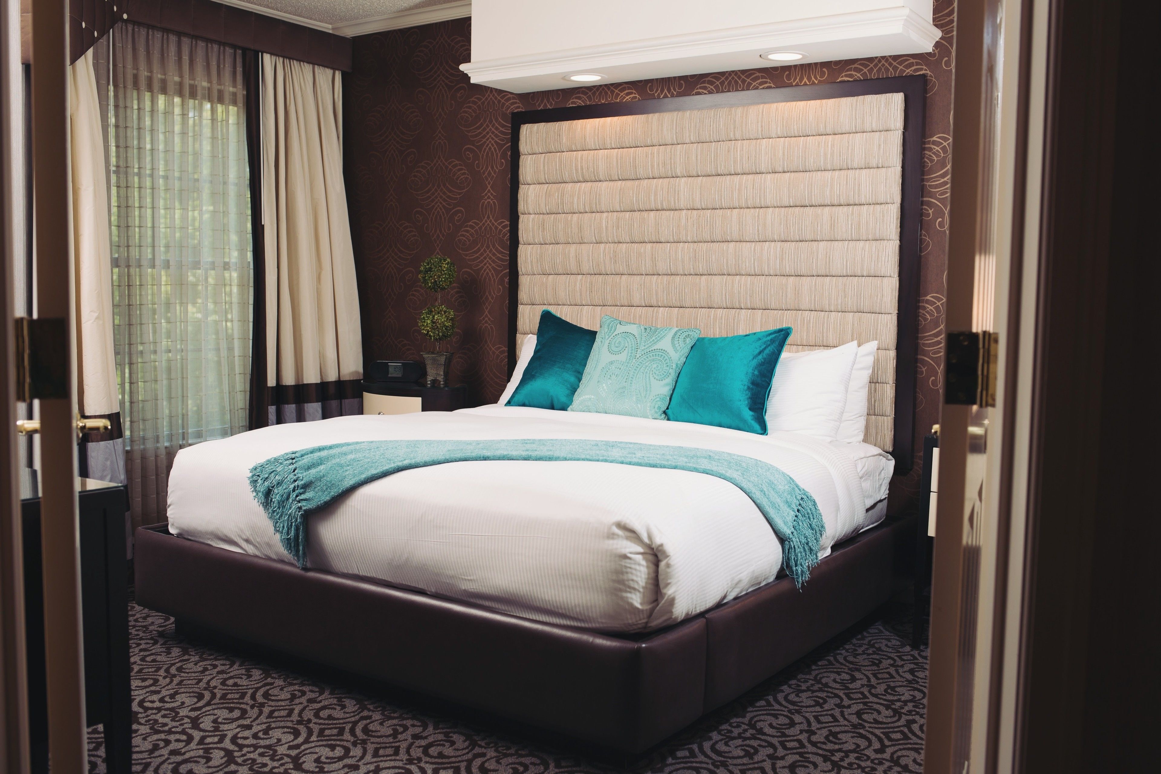 A large bed with a headboard, a bedside table, and a window with curtains.