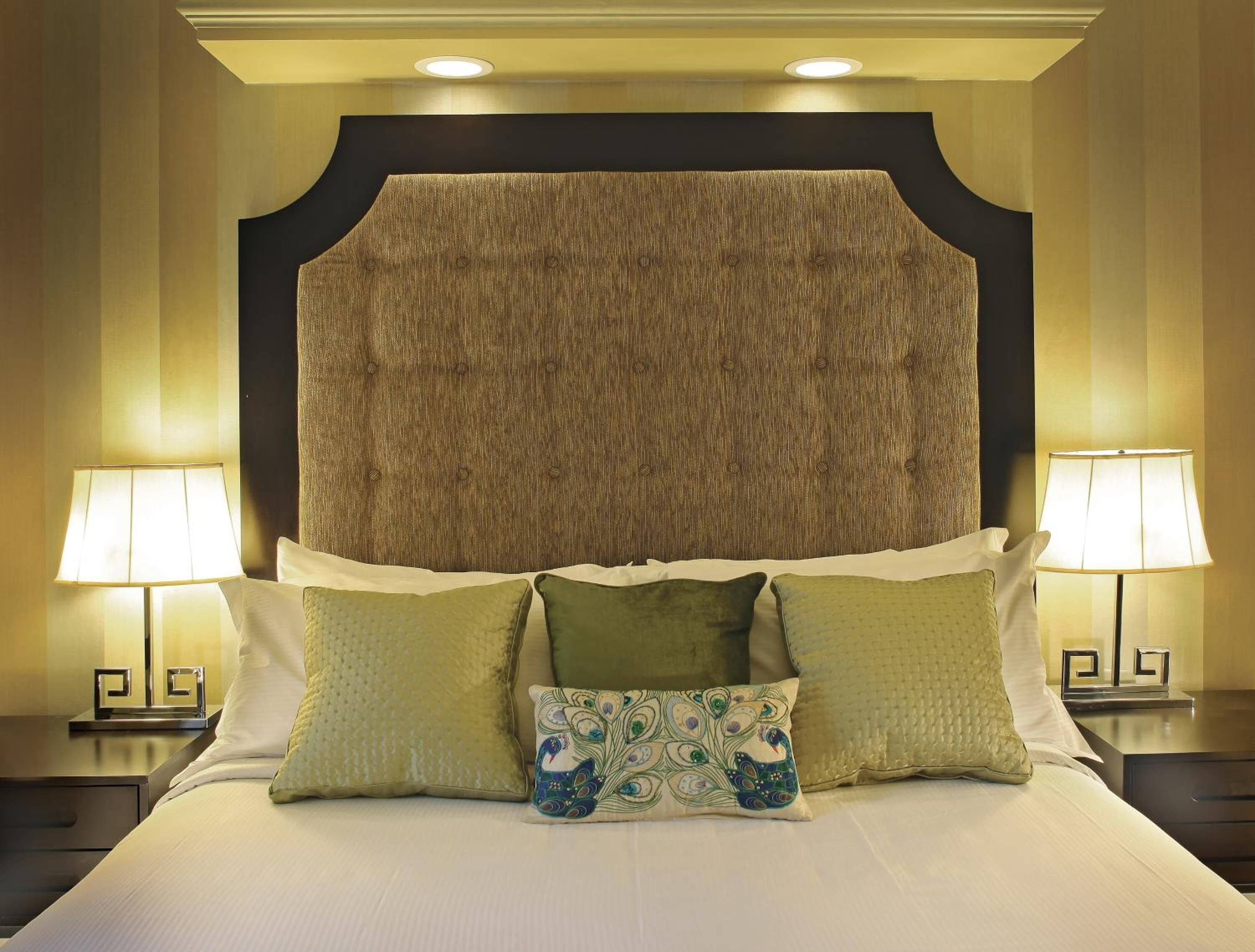 A hotel room with a large bed, two bedside lamps, and a decorative headboard.