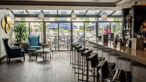 A bar area with a high ceiling, large windows, and a view of the outside. There are several chairs and tables, and a bar counter with stools. - The Inn At Fox Hollow Hotel (Woodbury)