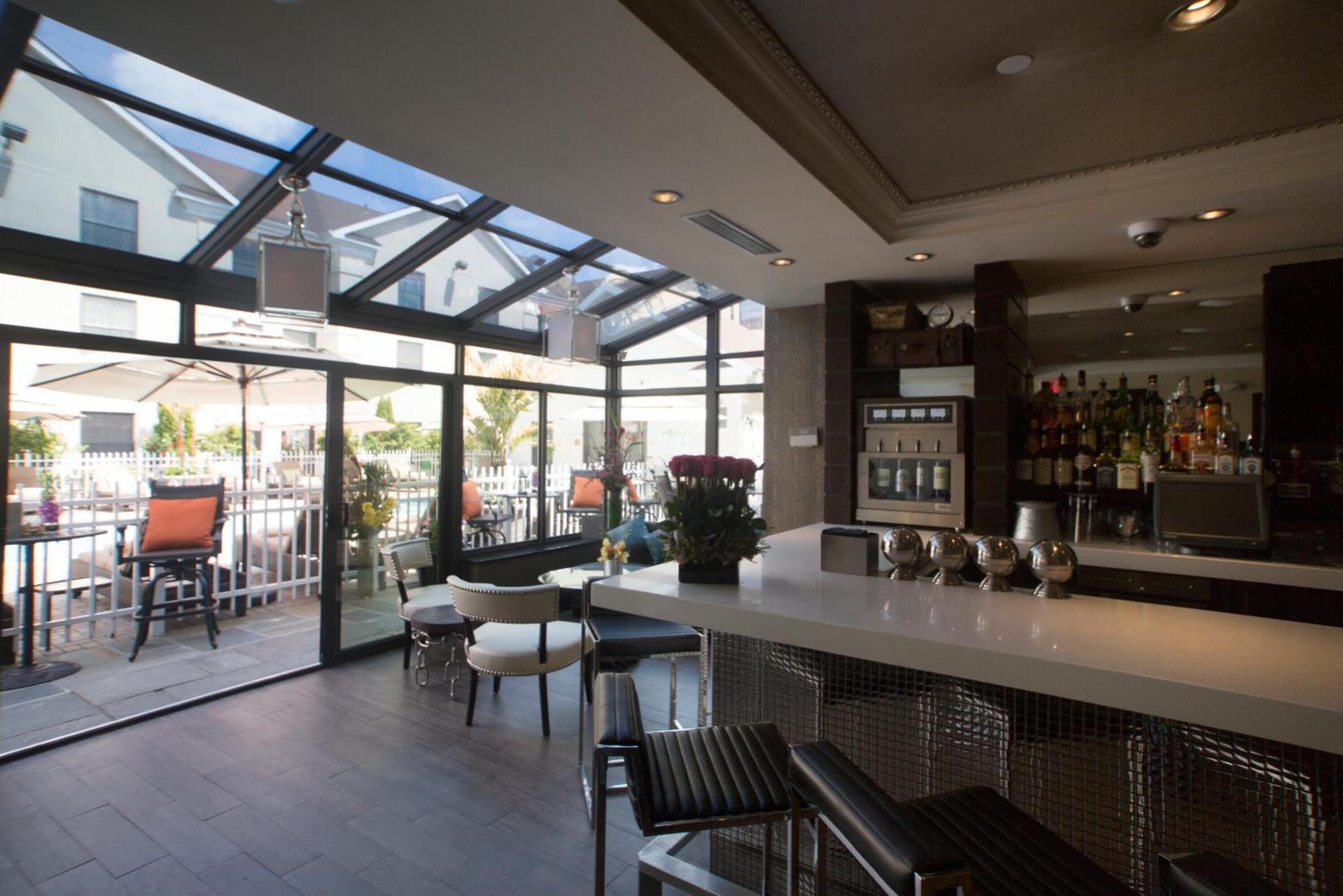 A modern bar area with a glass enclosure, seating, and a bar counter with various bottles.