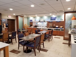 Una cafetería limpia y moderna con mesas y sillas de madera, una sección de panadería y una barra para el desayuno.