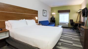 A hotel room with a large bed, a desk, a chair, a television, and a window with blinds.