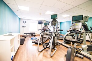 Un gimnasio con diversos equipos de ejercicio, como cintas de correr y bicicletas estáticas, y un mostrador de recepción.