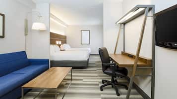 A hotel room with a blue sofa, a wooden desk, a computer, a chair, a bed, and a TV.