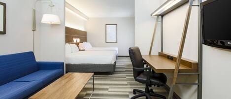 A hotel room with a blue sofa, a wooden desk, a computer, a chair, a bed, and a TV.