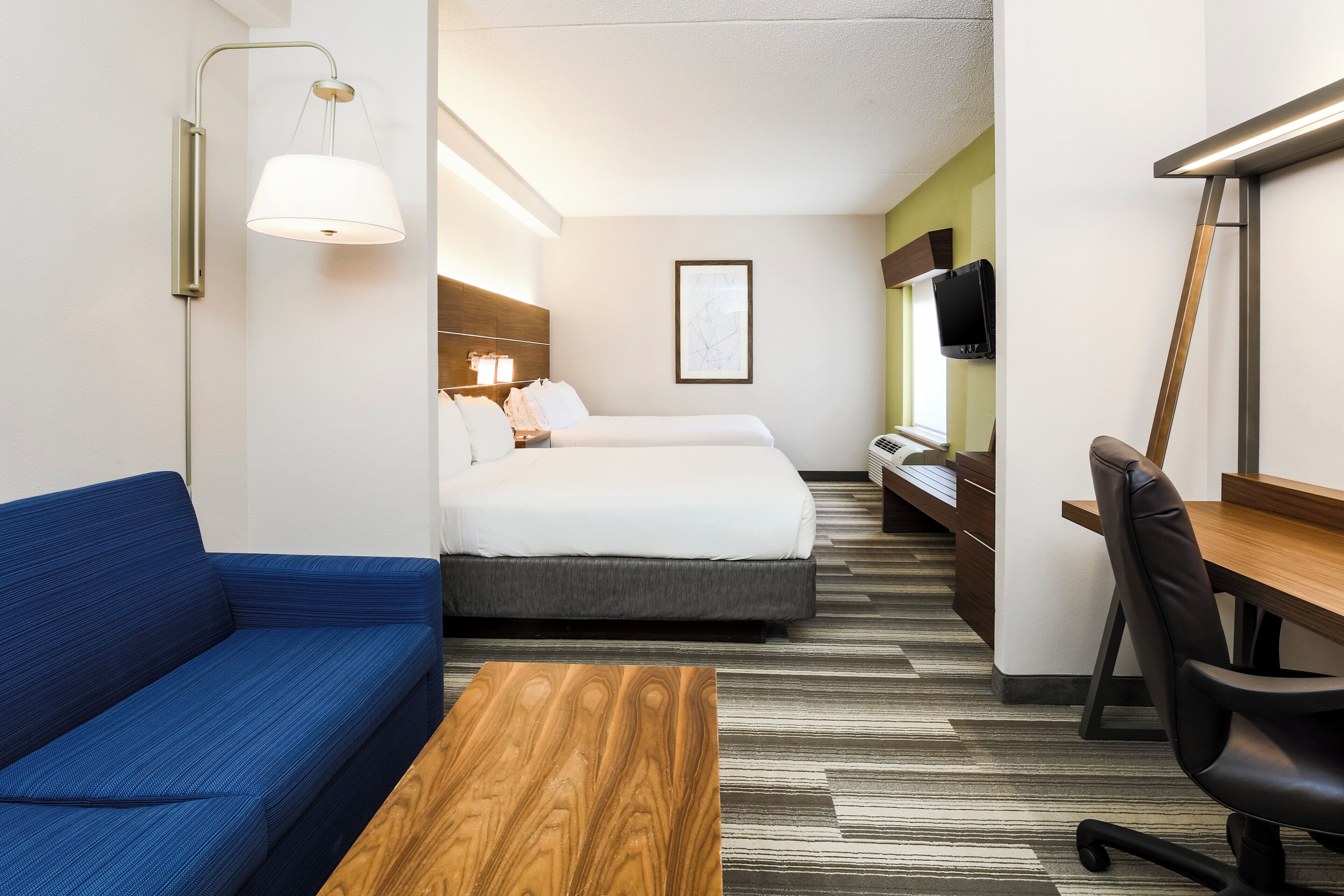 A hotel room with a bed, a desk, a chair, a sofa, and a television.