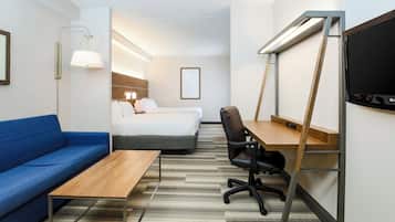 Quarto de hotel com cama, escrivaninha, cadeira, sofá e televisão.