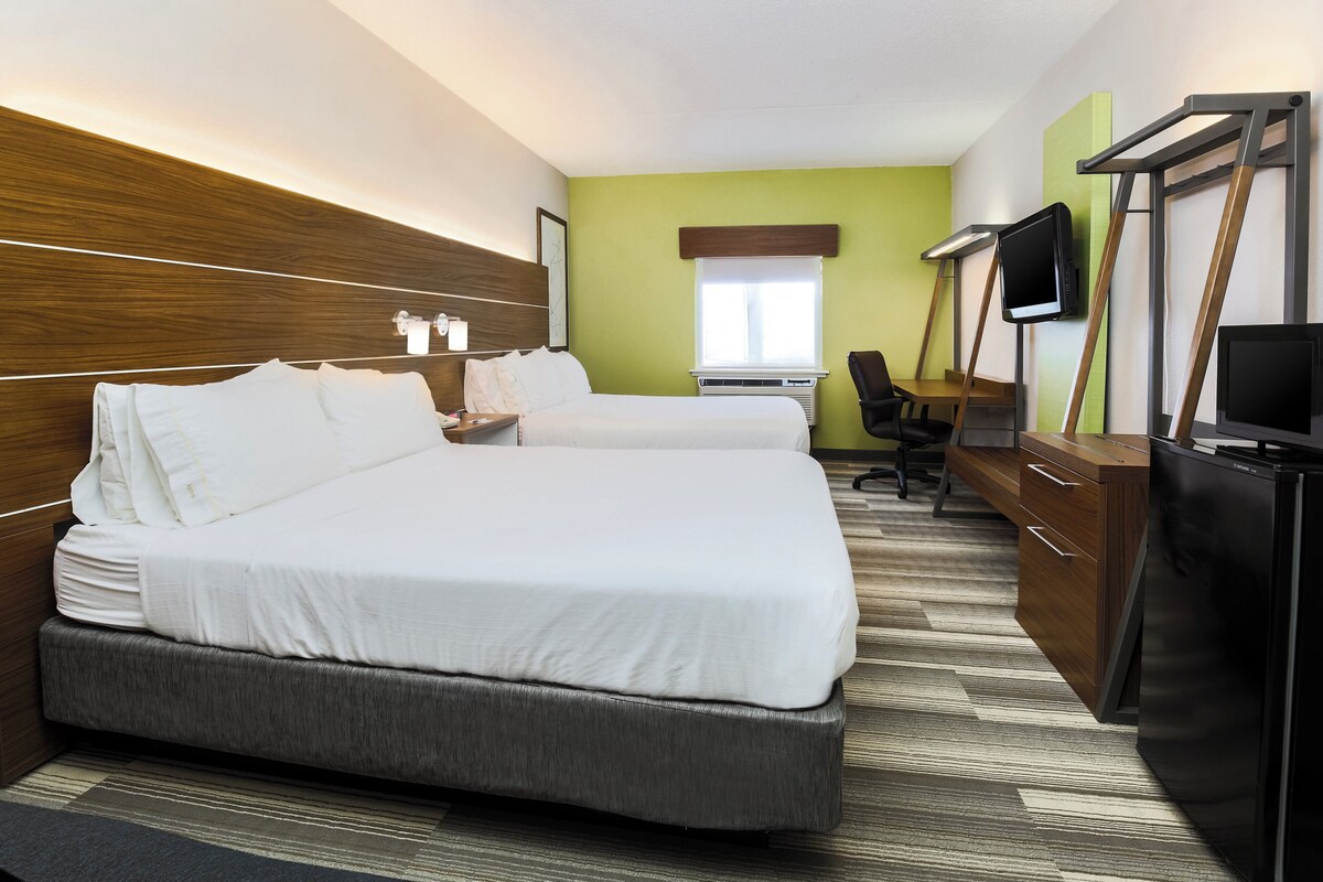 A hotel room with two beds, a desk, a chair, a TV, and a minibar.