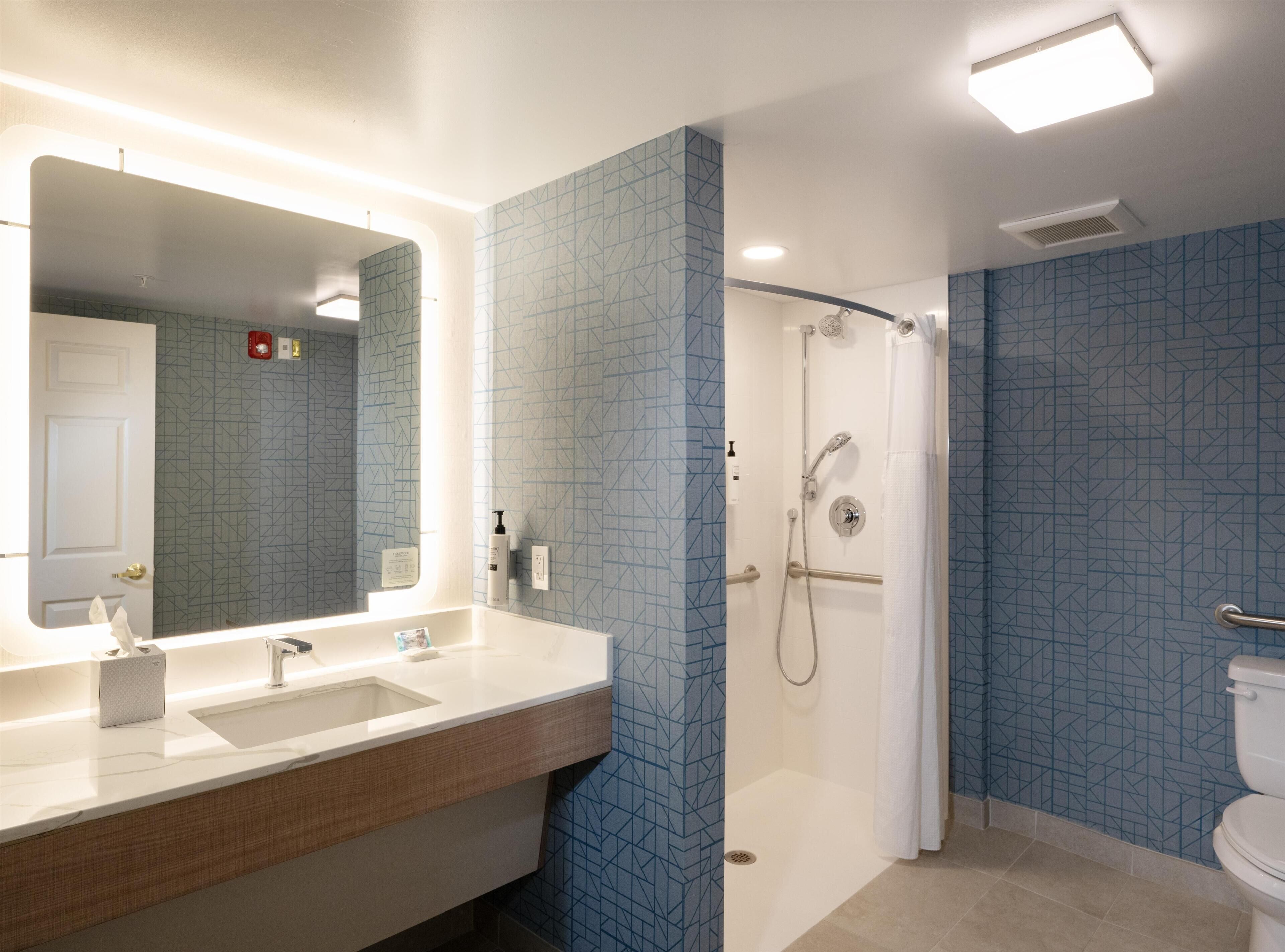 A modern bathroom with a large mirror, two sinks, a shower, and patterned blue walls.