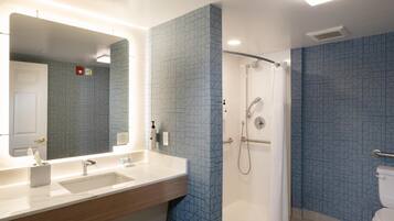 A modern bathroom with a large mirror, two sinks, a shower, and patterned blue walls.