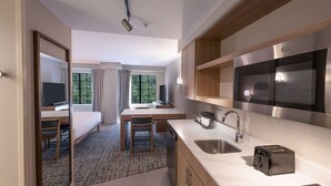 Une chambre d’hôtel de taille réduite, équipée d’une kitchenette, d’un lit, d’un bureau et d’une chaise.
